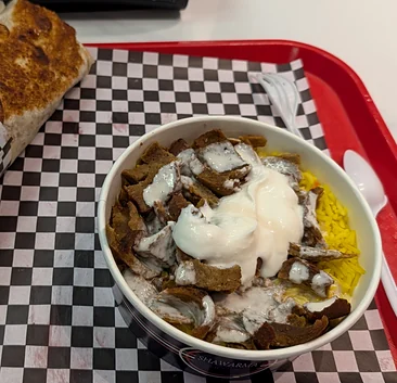 Beef donair over yellow rice with garlic sauce on a checkered tray
