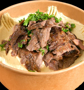 Hummus topped with beef shawarma and parsley in a paper bowl