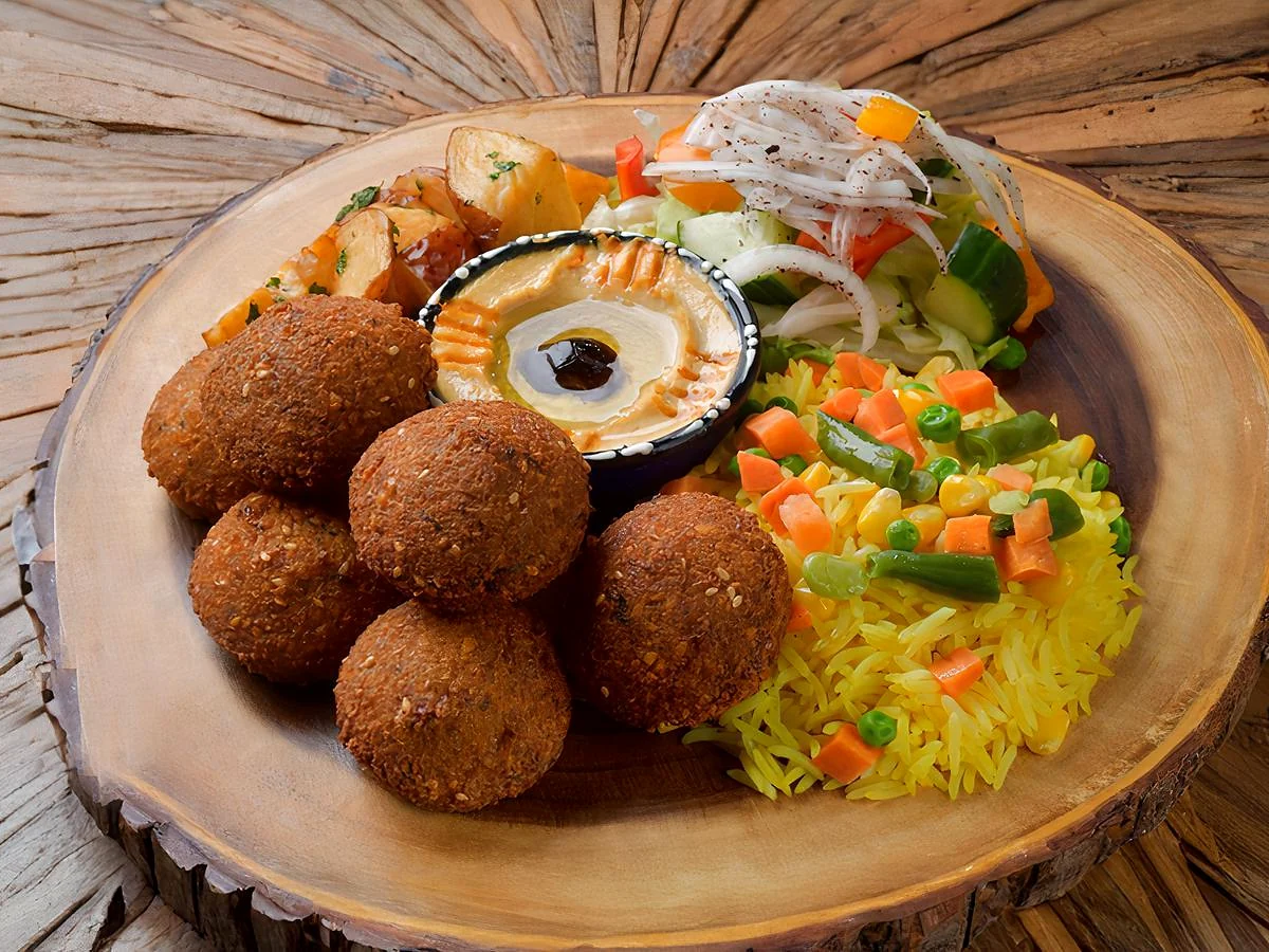 Falafel with hummus, yellow rice, garlic potatoes and salad on a wooden board